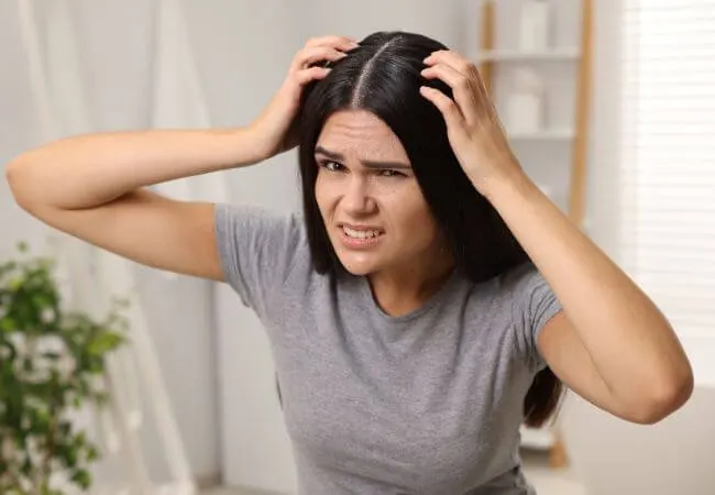 A woman examining flaking and irritation on her scalp.